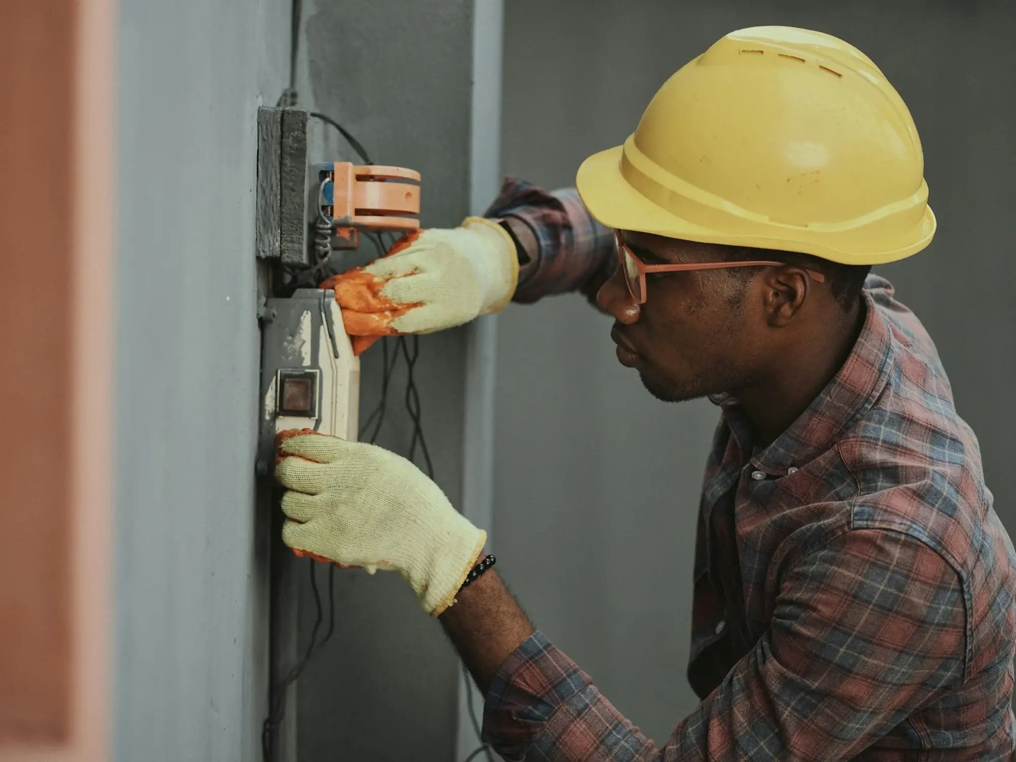 Técnico de capacete e luvas fazendo manutenção em um quadro elétrico na parede externa de um cliente