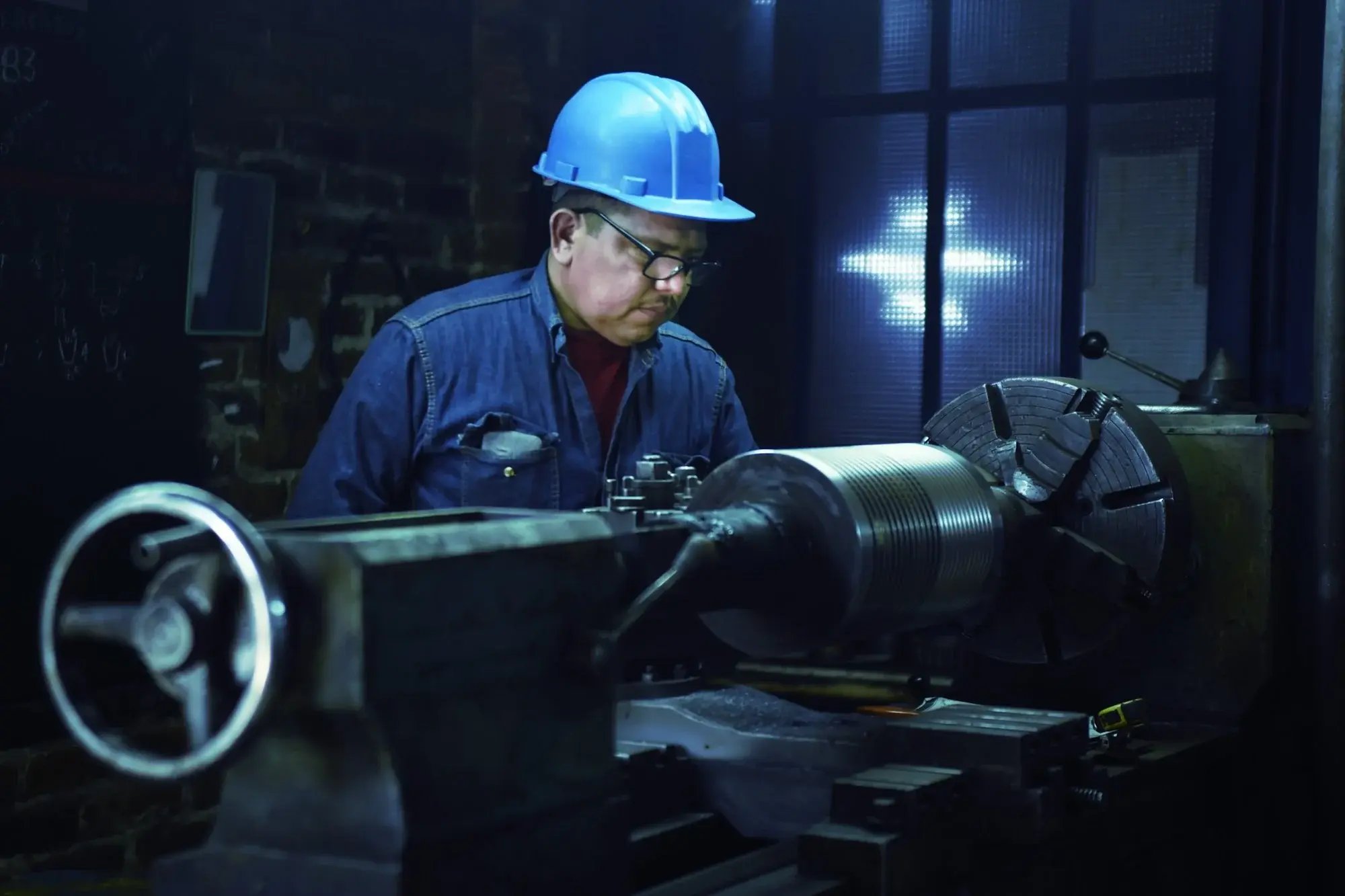 Operador de capacete azul trabalha em um torno em uma oficina industrial