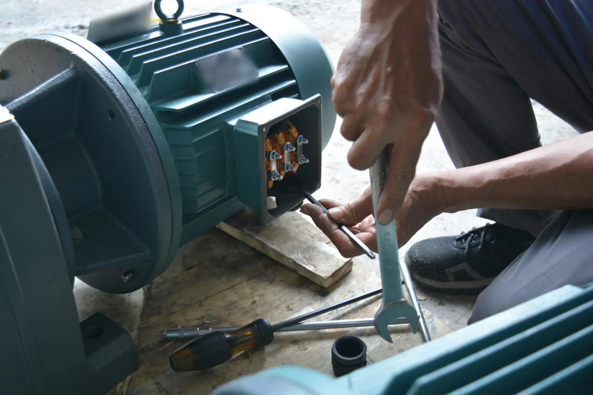 Técnico de mantenimiento ajustando las conexiones en la caja de bornes de un motor eléctrico industrial