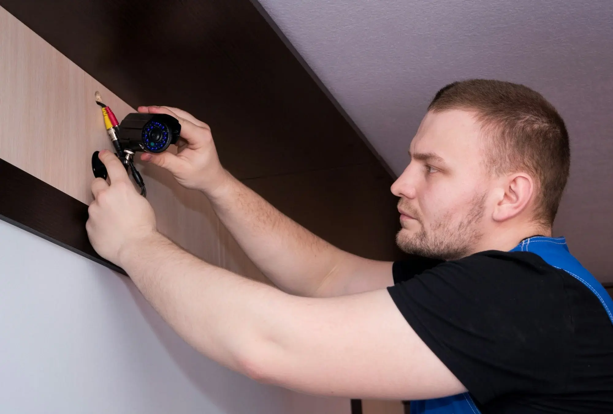 Técnico de seguridad electrónica fijando y conectando una cámara de CCTV en la pared