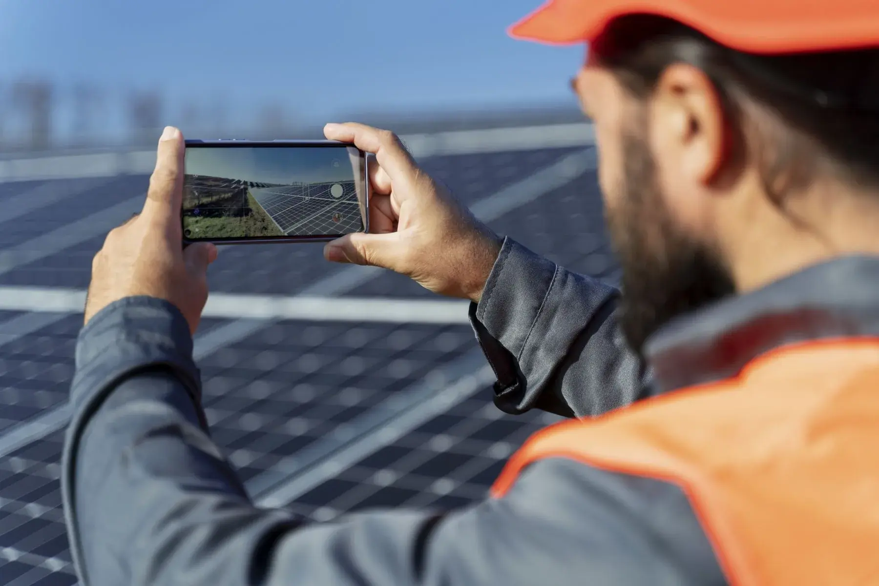 Técnico con chaleco naranja fotografiando con el celular los módulos de una planta solar fotovoltaica